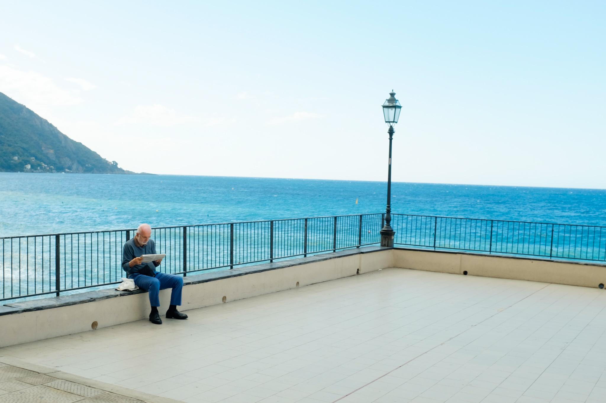 ein Mann sitzt auf einer Bank mit dem Rücken zum Meer und liest in einer Zeitung